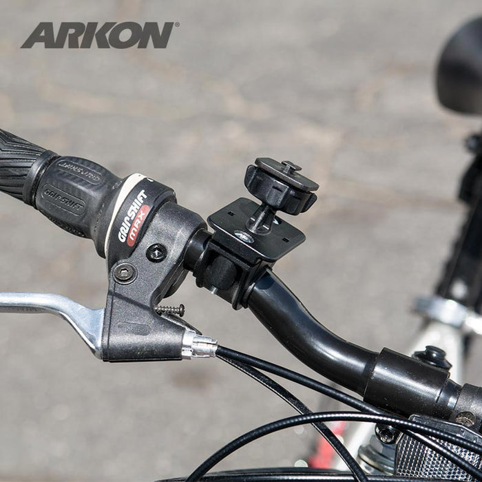 Close-up of a bicycle handlebar with a gear shifter, brake lever, and a Bike or Motorcycle Handlebar Mount for XM Satellite Radio (compatible with Bracketron, Scosche). Blurred pavement in the background.