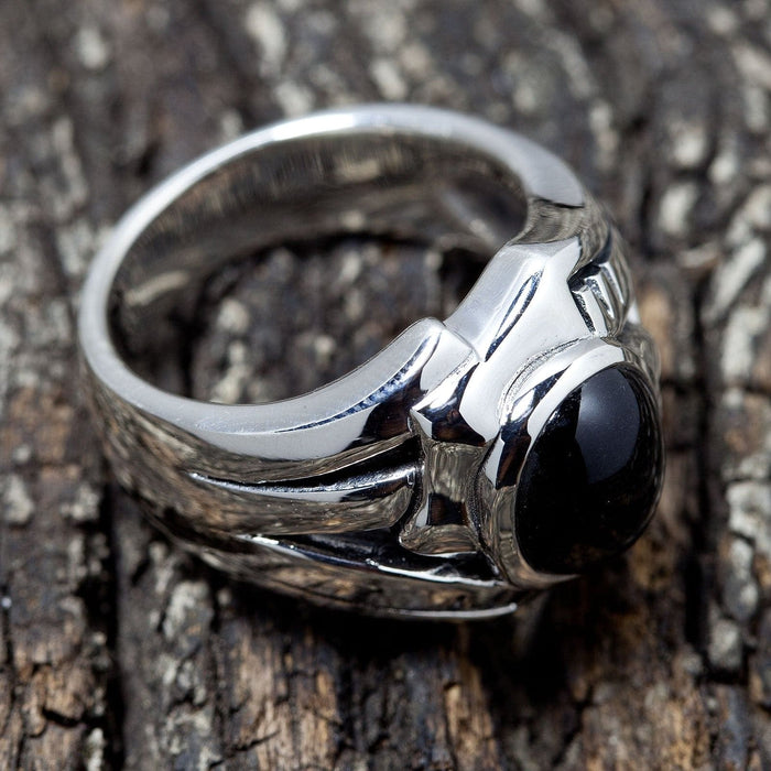 Sculpted side grooves on the thick sterling silver band, angled to show the smooth black stone against rough wood bark.