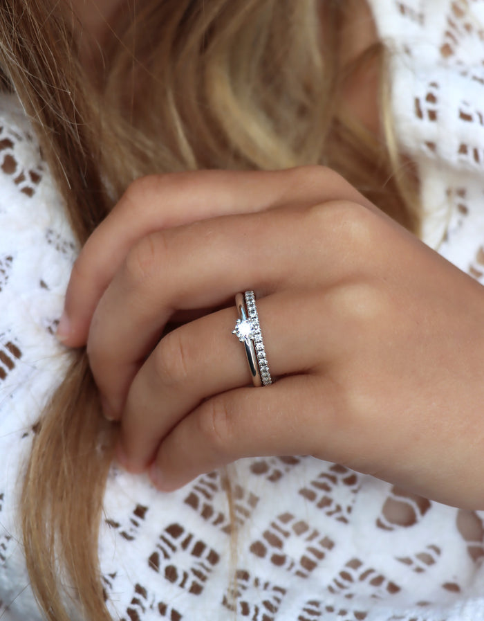 Tjej som bär två diamantringar som vigsel- och förlovningsring. Silverringar med diamanter. En alliansring med flera små diamanter och en ring med en diamant 0,25 ct.