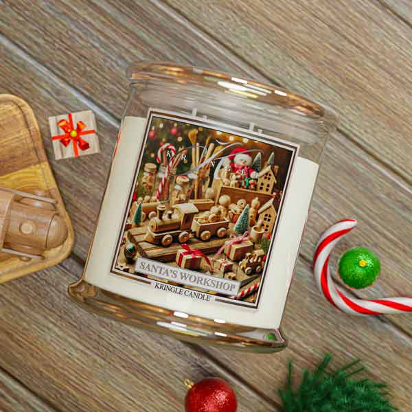 Kringle Candle jar with 'Santa's Workshop' design on a wooden surface with Christmas decor.