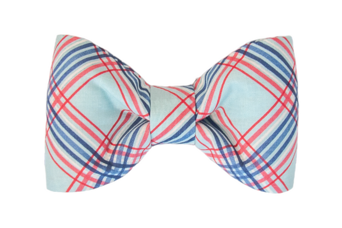 Close-up of a neatly tied plaid bow tie for your pup in light blue with intersecting red, white, and navy blue lines. The design has a crisp, preppy aesthetic.