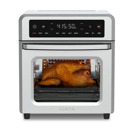 Cosori 13-Quart Air Fryer Oven with a whole roasted chicken cooking inside. Stainless steel finish