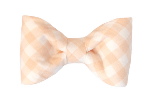 Apricot and white checkered fabric bow tie with subtle curves and a gathered center, made from lightweight cotton and designed for dog collars. The structured yet plush appearance gives it a polished but playful vibe.