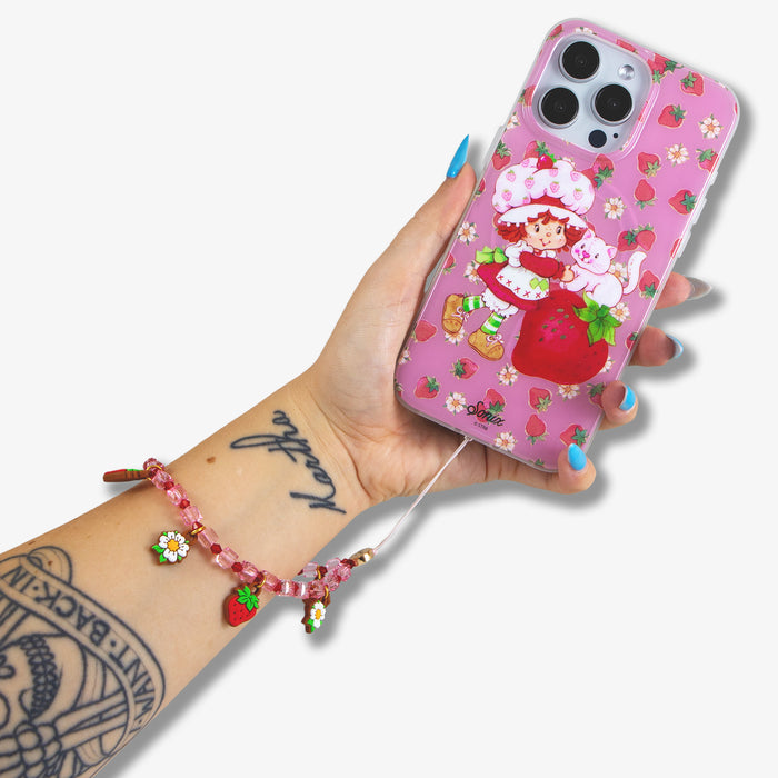 Close up of beaded wristlet with charm showcasing pink faceted beads and strawberry and daisy charms attached to a phone on white background