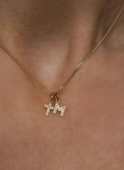 Kvinna som bär ett halsband med ett diamantkors i guld och en bokstavsberlock i guld med diamanter.
