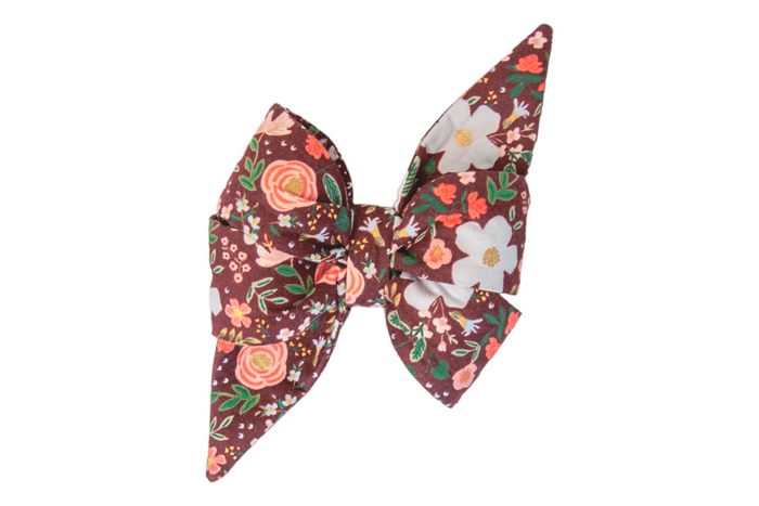 Stylish fabric belle bow for a dogs in a deep burgundy, covered with a dense botanical print of roses, daisies, blossoms, and other scattered small flowers, with vibrant foliage, cinched at the center for a neat, crisp finish.