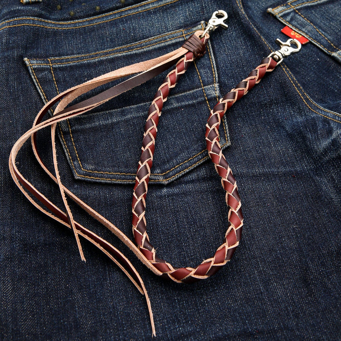 The braided leather wallet strap in a loop, showing the tribal zigzag braid pattern and lobster clasps on jeans.