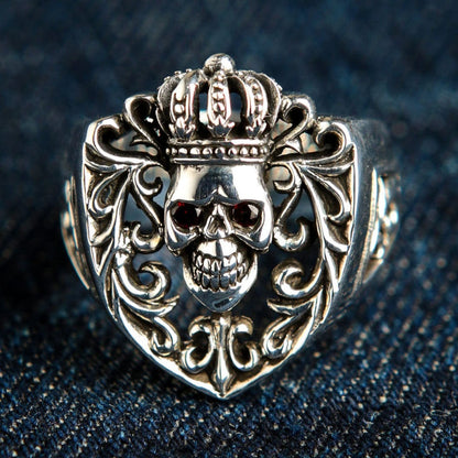 Front view of the Crown Sterling Silver Skull Ring featuring red garnet CZ eyes and ornate gothic scrollwork on dark denim.