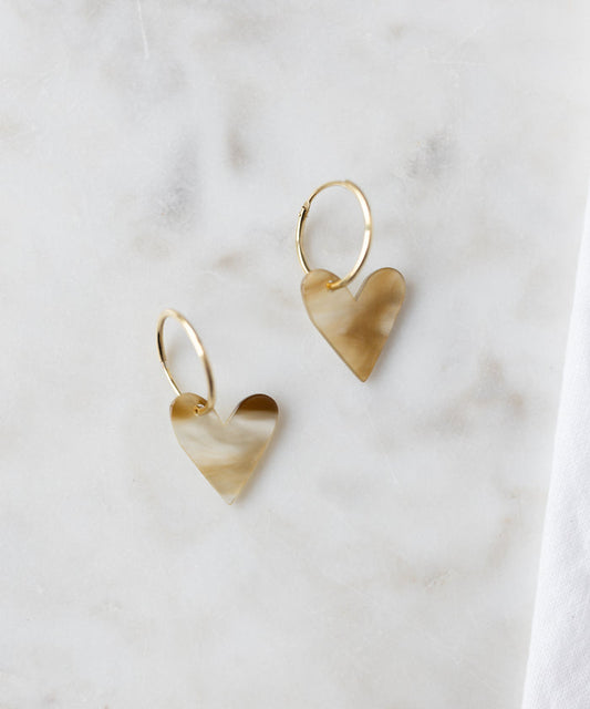 The WALD Berlin Exclusive Heart Black Earrings feature recycled gold hoops with marbled black heart-shaped pendants, elegantly displayed on a light marble surface.