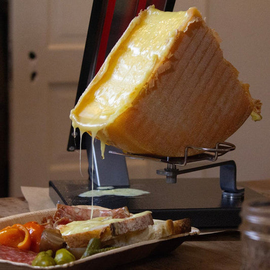 A quarter raclette wheel partially melted and dripping onto bread.
