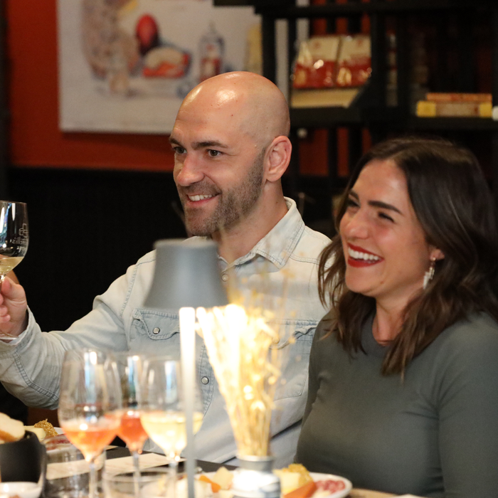 Man and woman sitting at a table with wine glasses, smiling and enjoying a meal.