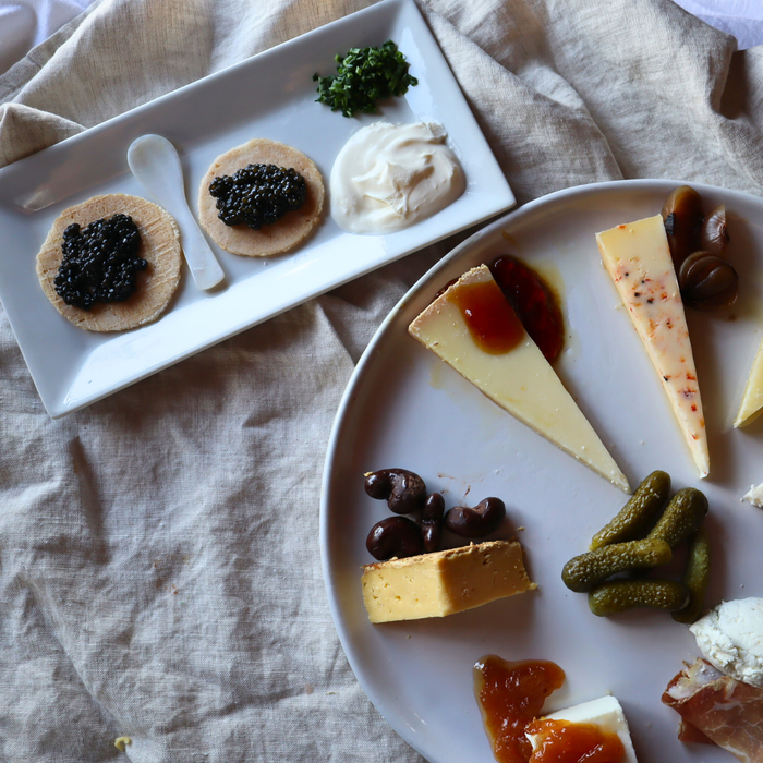 Plates of assorted cheeses, pickles, and other snacks on a textured fabric background