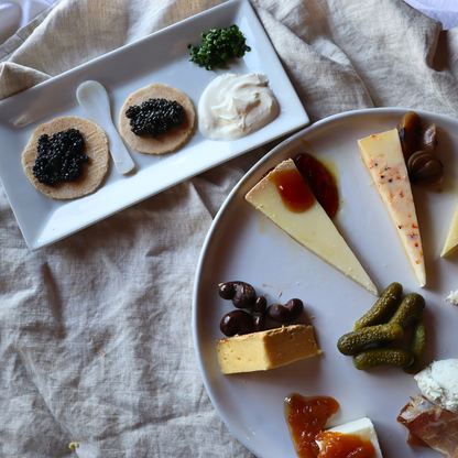 Plates of assorted cheeses, pickles, and other snacks on a textured fabric background