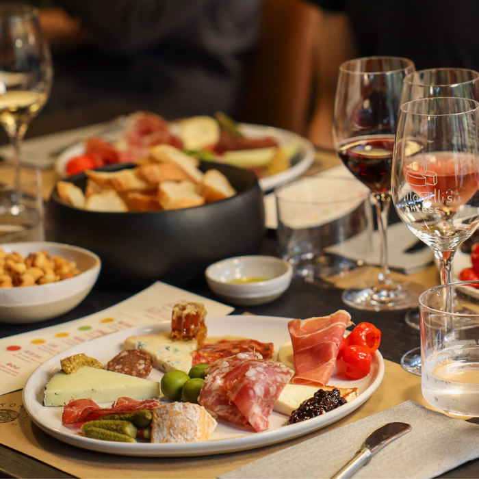 Platter of assorted meats, cheeses, and vegetables with wine glasses on a table.