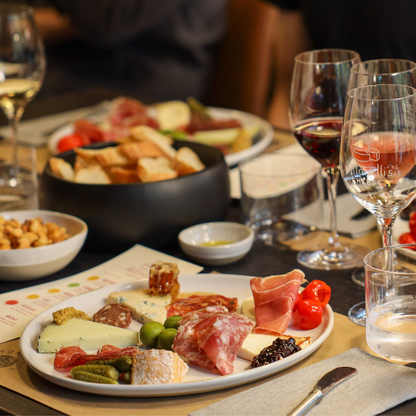 Platter of assorted meats, cheeses, and vegetables with wine glasses on a table.