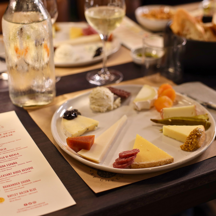 Plated assortment of cheeses and cured meats with a glass of white wine on a table.