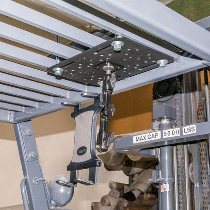A Forklift Slim-Grip® Tablet Mount is bolted under a metal platform near machinery, positioned above a MAX CAP 5000 LBS sign, with various mechanical components visible in the background.