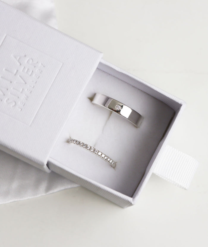 Ett set med vigsel/förlovningsringar i silver med diamanter. Ringarna presenteras i en vit ringask.