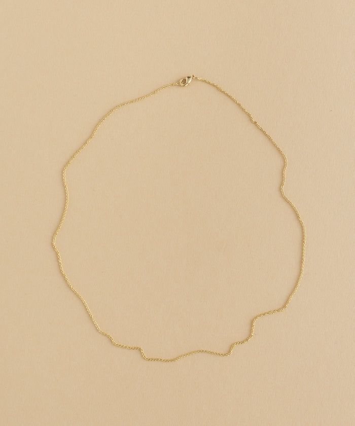 A gold necklace with a charm pendant on a beige background.