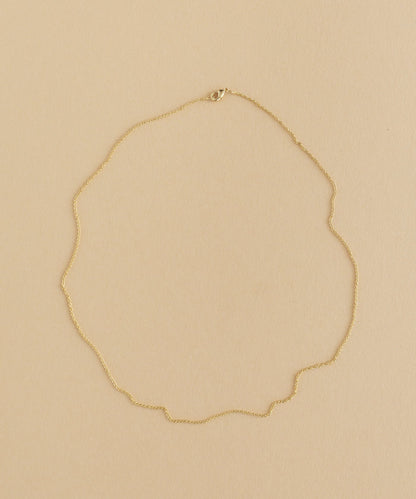 A gold necklace with a charm pendant on a beige background.