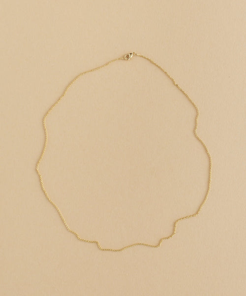 A gold necklace with a charm pendant on a beige background.