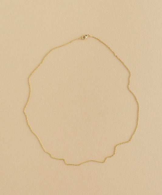 A gold necklace with a charm pendant on a beige background.