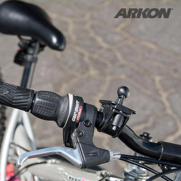 Close-up of a bicycle handlebar with black rubber grip, gear shifter, brake lever, and a Bike or Motorcycle Handlebar Mount for Garmin nuvi 40, 50, 200, 2013, 24x5, 25x5 GPS. Paved surface in the background.