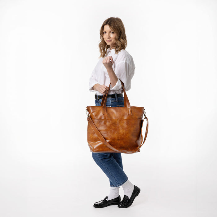 Brown leather tote bag next to blue denim jeans on a neutral background