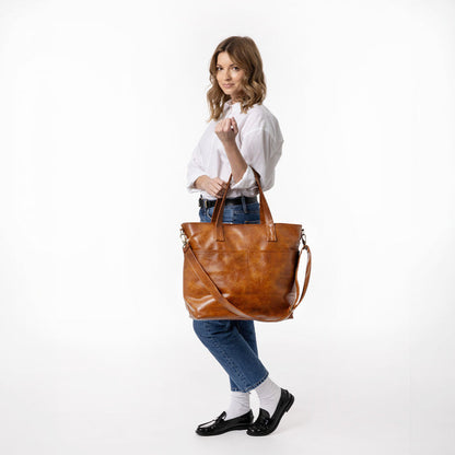 Brown leather tote bag next to blue denim jeans on a neutral background