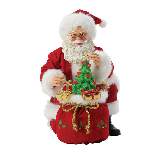 A figurine of Santa Claus with a vintage ceramic Christmas tree with presents, wearing his traditional red and white outfit.