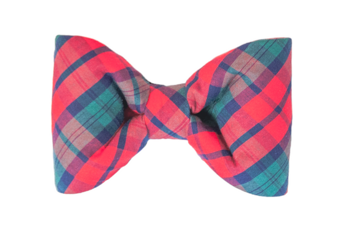A plaid fabric bow tie with bold red checks. The bow has a symmetrical, puffed shape with subtle pleats and a centered knot, ideal for formal or festive wear. The soft fabric appears slightly cushioned, maintaining its form while remaining flexible.
