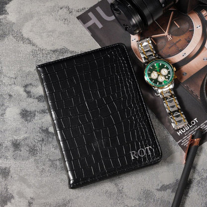 Black crocodile-patterned wallet with 'ROT' branding on a textured surface, next to a Hublot watch.