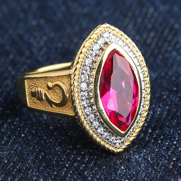 Close-up side angle revealing a raised crosier emblem on the textured gold band beside the prominent marquise red ruby.