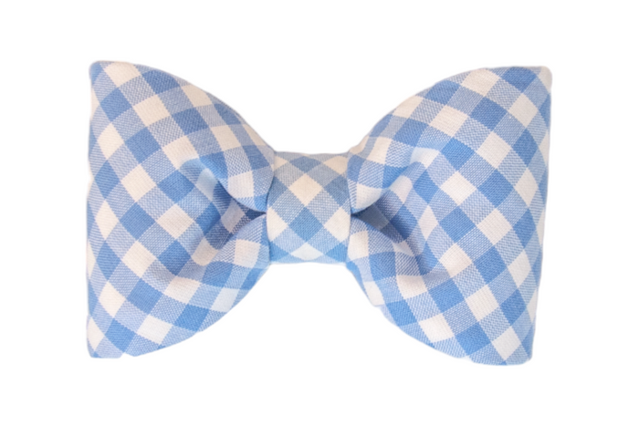 Dog bow tie crafted from lightweight cotton in a periwinkle and white plaid check. The bow tie is neatly pleated and sewn to maintain a classic silhouette, with a band of the same fabric cinching the center. The fabric’s subtle texture and the sharp contrast between white and periwinkle create a charming, timeless design.