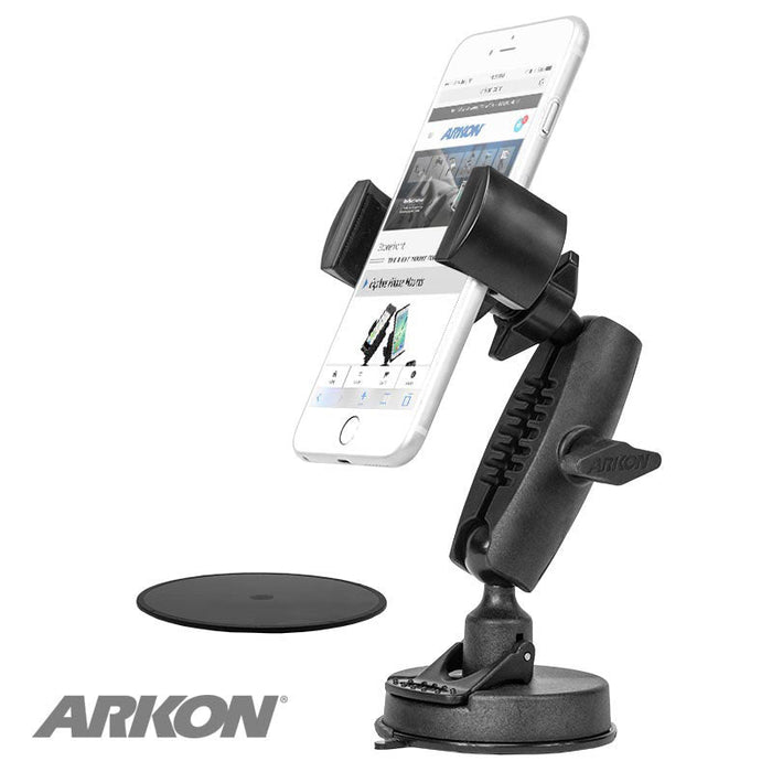 The black RoadVise® Phone Holder with Sticky Suction Mount and Shaft keeps a smartphone upright. Its adjustable arm and suction cup make it ideal for beauty content creators. A round adhesive pad is nearby, with the Arkon logo visible in the lower left corner.