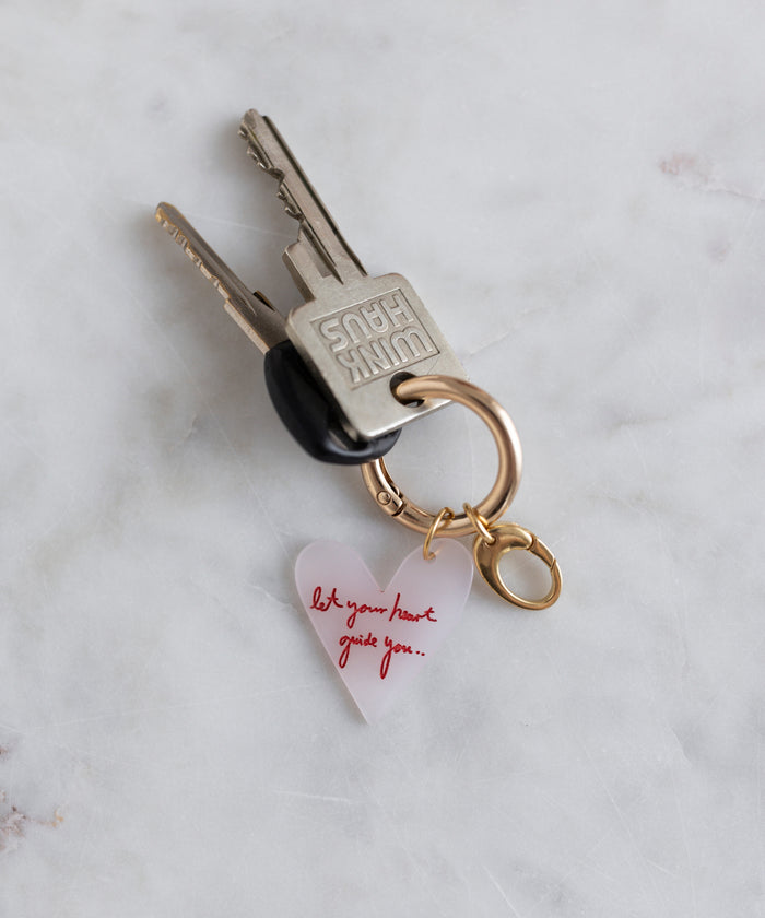 The WALD Berlin SAMPLE SALE Love Key Chain features keys on a gold ring with a clear, heart-shaped charm reading "let your heart guide you" in red script, displayed on white marble. Made in Germany.
