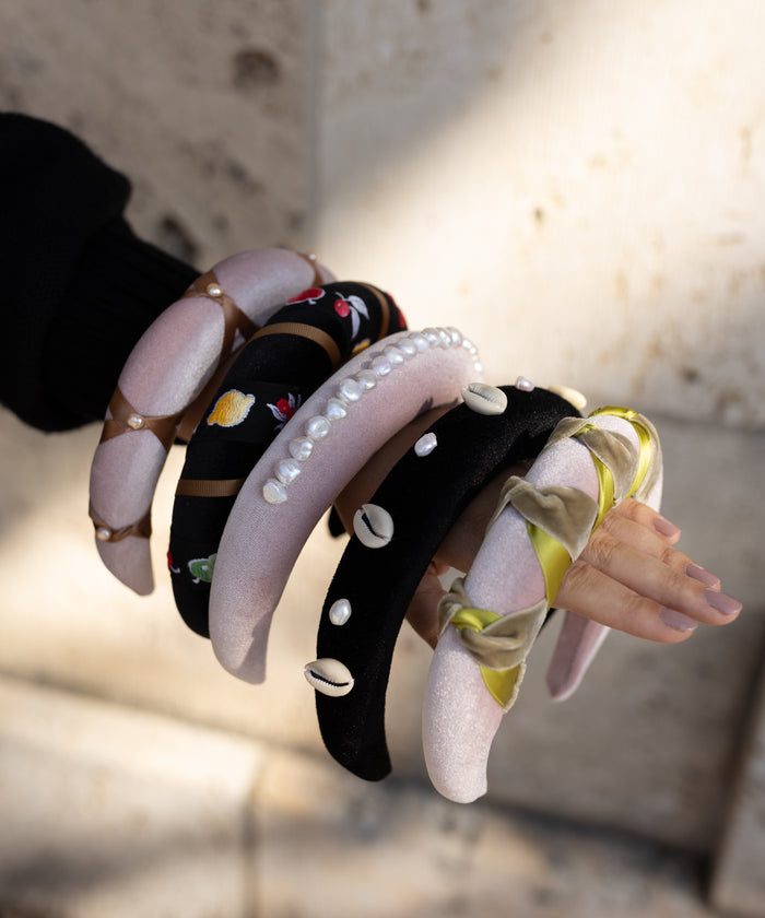 An arm stacked with multiple WALD Berlin headbands, including the SAMPLES SALE Lady Di Headband Rose, featuring velvet, pearls, shells, embroidery, and ribbons from wrist to fingertips.