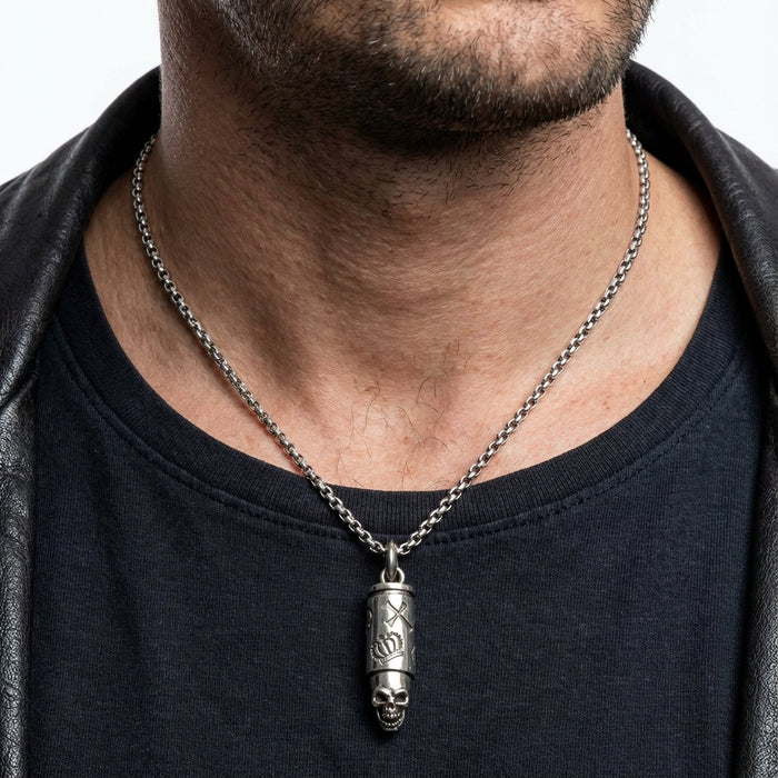 Close-up of a man wearing a sterling silver skull bullet pendant necklace on a silver chain against a plain studio background.