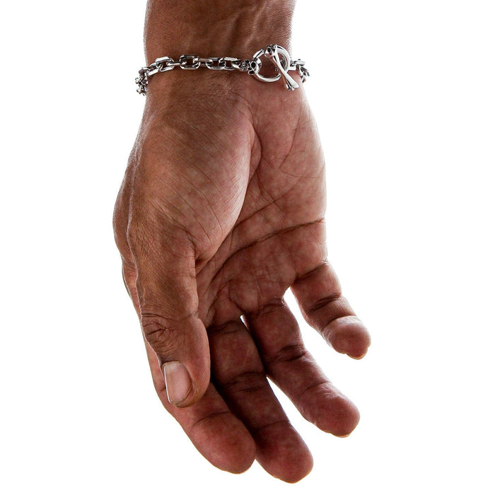 A man's hand with the silver link bracelet hanging to show the skull clasp detail.