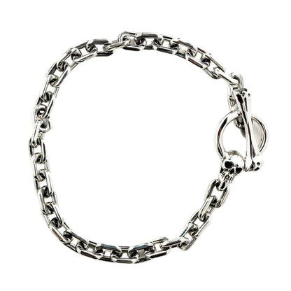 The polished sterling silver chain bracelet with skull T-bar clasp, laid in a curved shape.