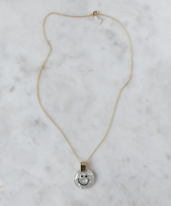 The WALD Berlin Smilie Dude Medaillon Pearl Necklace features an 18k gold-plated chain and round pendant with a smiley face on a white marbled background, adding cheerful spring colors to any outfit.