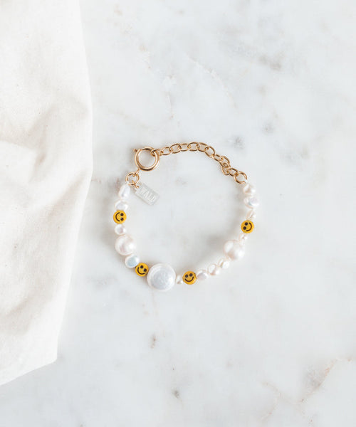 The WALD Berlin Smilie Dude Pearl Bracelet with Extention is showcased on a marble surface, featuring sweetwater pearls and cheerful smiley beads.