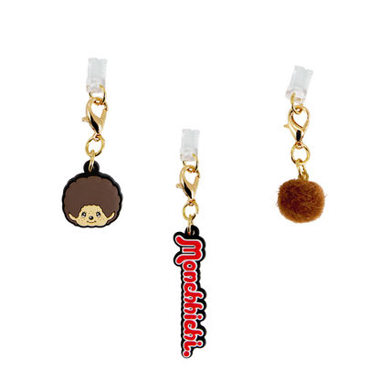 Front close-up of Monchhichi charging port charms 3-pack showing gold clasps, character face and brown pom pom on white