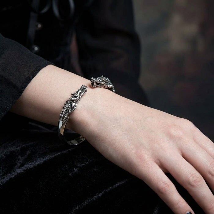 Sterling silver dragon cuff bracelet with intricate Celtic-inspired scrollwork design worn on a woman's wrist against black velvet fabric background