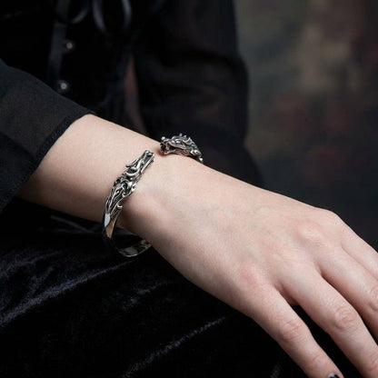 Sterling silver dragon cuff bracelet with intricate Celtic-inspired scrollwork design worn on a woman's wrist against black velvet fabric background