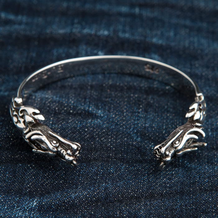 A solid 925 sterling silver dragon cuff bracelet with two dragon heads, shown on a denim background.