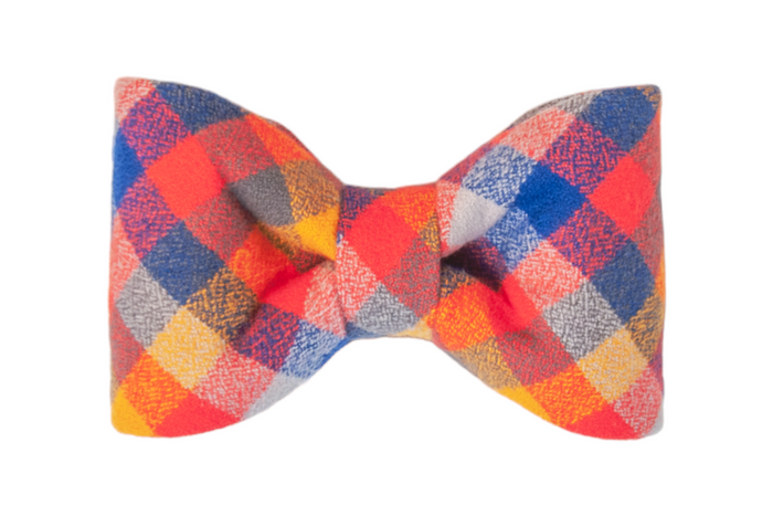 Colorful plaid bow tie featuring intersecting blocks of red, blue, orange,  crafted from soft flannel fabric and folded into a balanced, classic, double-loop shape.