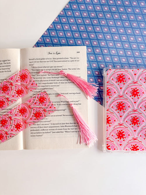 Open book with a pink and red patterned bookmark and notebook on a blue and white patterned fabric background.