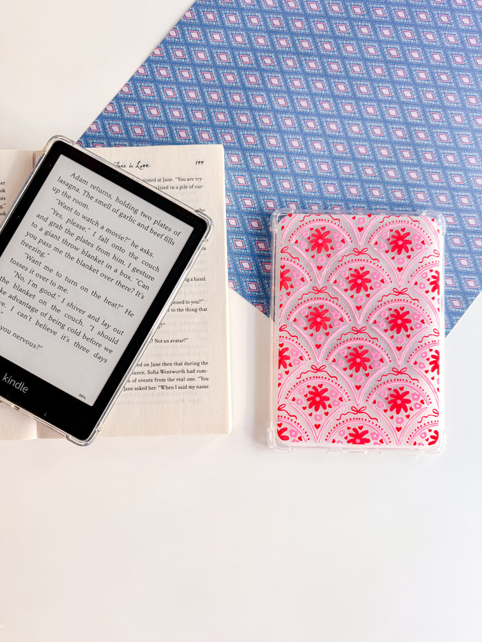 Kindle device, open book, and pink patterned notebook on a blue and white checkered fabric background