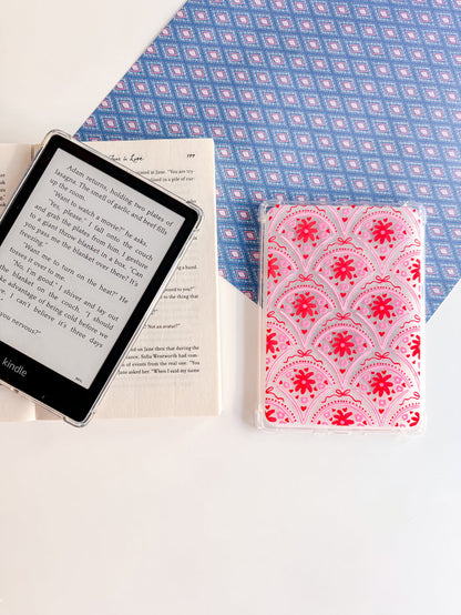 Kindle device, open book, and pink patterned notebook on a blue and white checkered fabric background